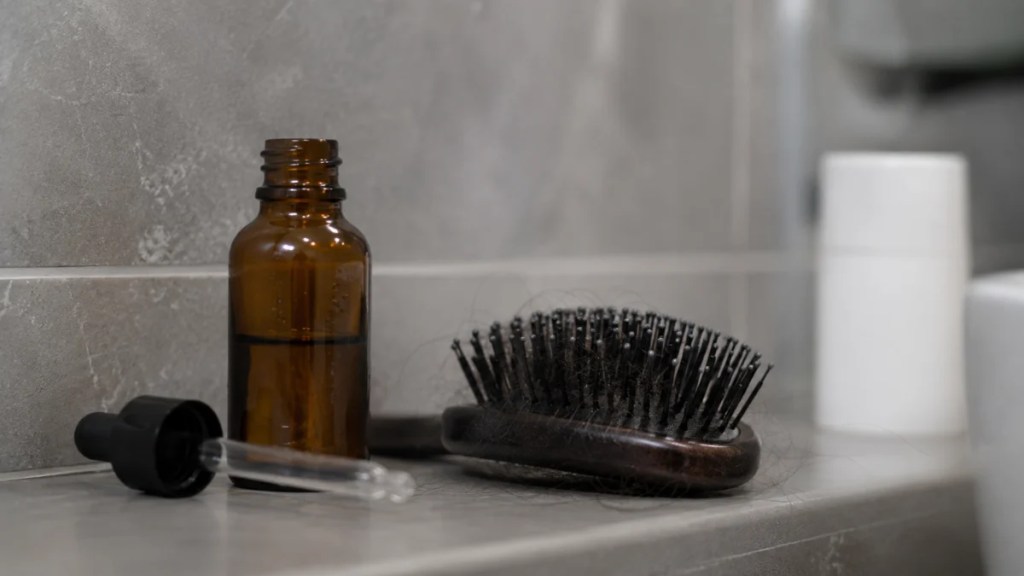 Hairbrush with shed hair strands showing rebound hair fall after stopping minoxidil, leading users to a non minoxidil hair growth serum